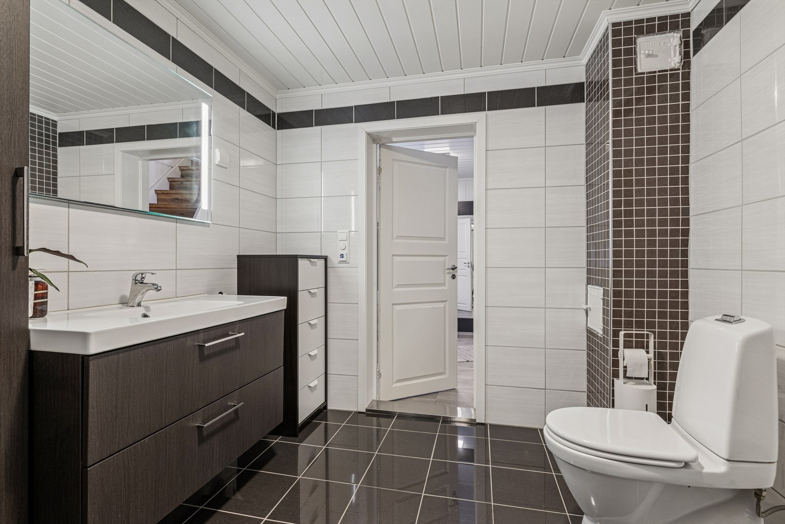 Romslig baderom med flislagte overflater, moderne innredning og god plass til oppbevaring. Rommet har både vegghengt speil med belysning og praktisk servantinnredning Galleribilde