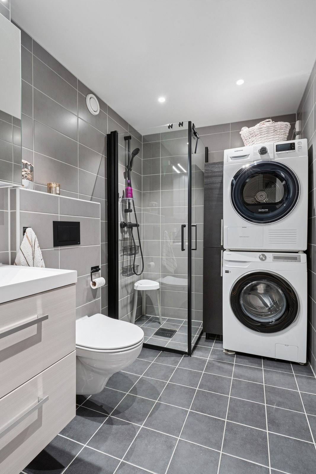 Baderommet er innredet med vegghengt toalett, servant med to underskuffer, speilskap med belysning, dusjnisje med innfellbare glassdører, og opplegg for en praktisk vaskesøyle i hjørne Galleribilde