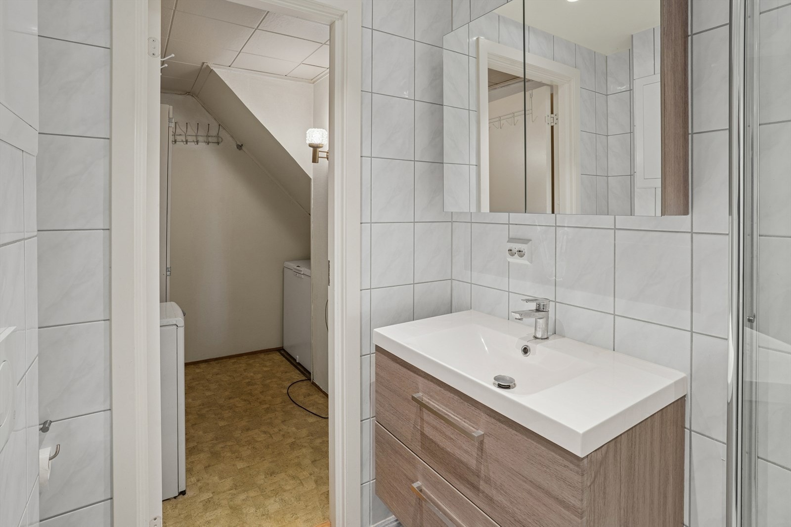 Badet er innredet med servantskap med ett-greps blandebatteri, speilskap, vegghengt toalett med innebygget sisterne, avskjermet dusjhjørne med glass, blandebatteri og dusjgarnityr. Galleribilde