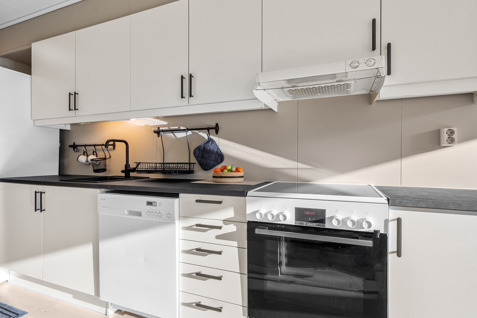 Pent kjøkken med ny sort benkeplate fra 2026, sort nedfelt kum, sort blandebatteri og lys under overskap Galleribilde