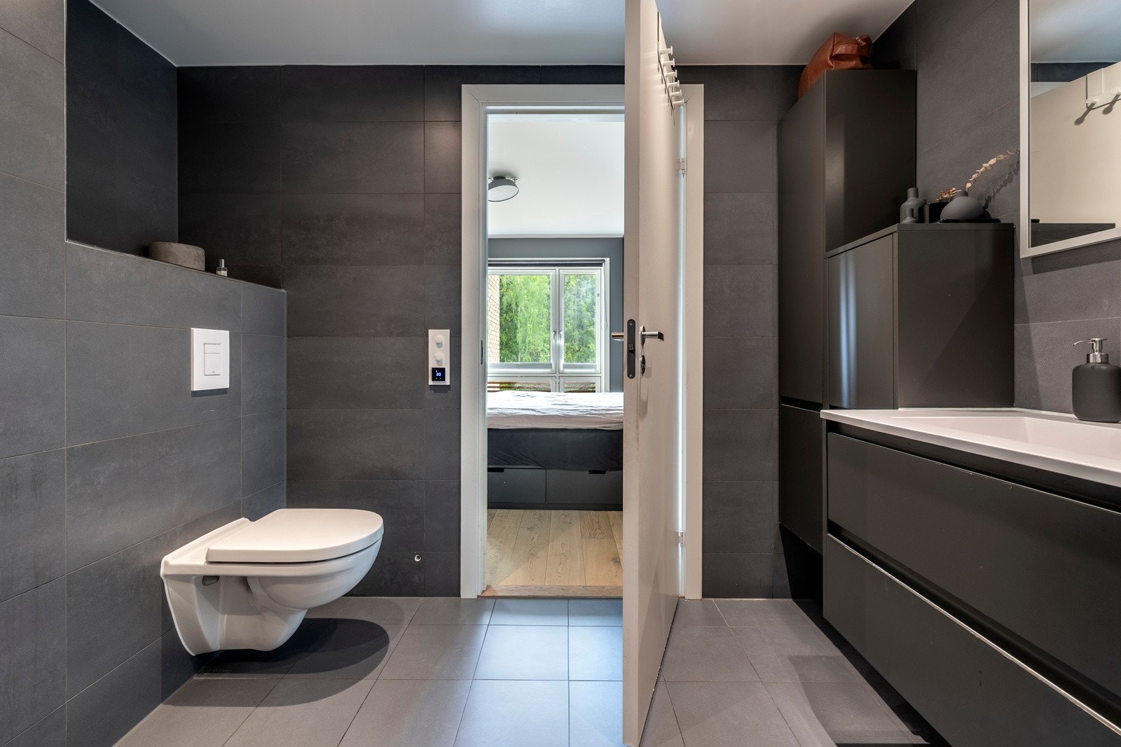 Badet har et stilrent utrykk med store vegg- og gulvfliser i grå toner, downlights, varmekabler og balansert ventilasjon. Galleribilde