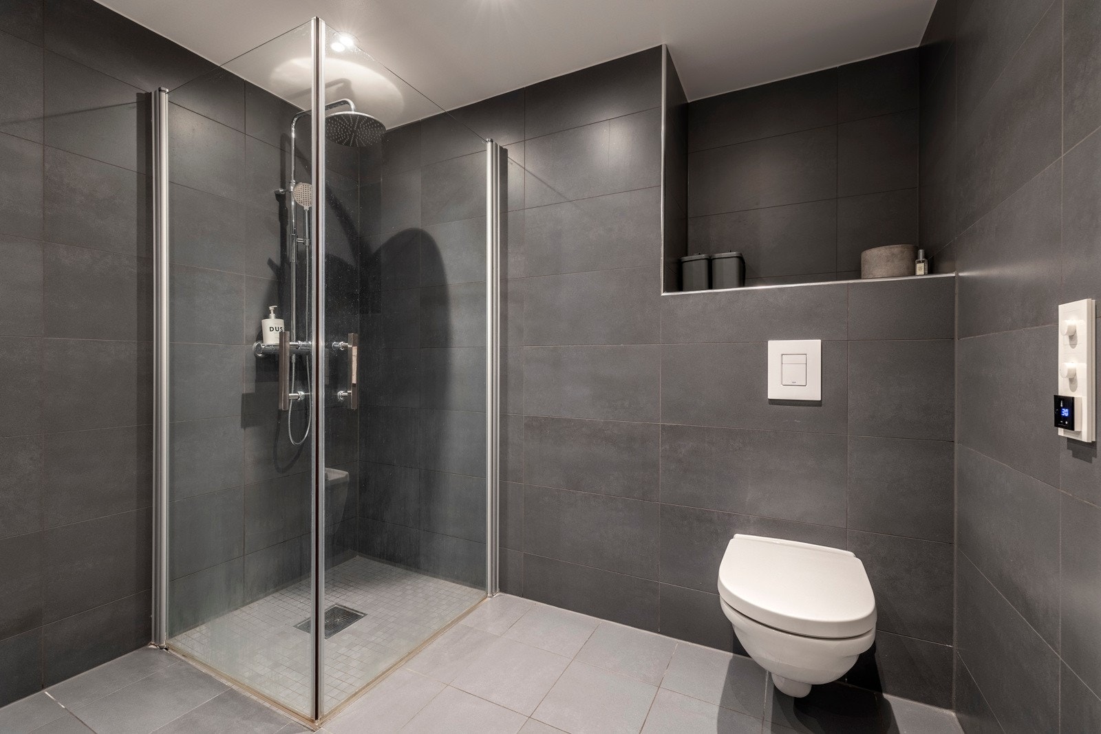 Innredet med servantinnredning, speil med lys på vegg over servant, vegghengt toalett, dusjhjørne med svingbare glassdører og opplegg for vaskemaskin. Galleribilde