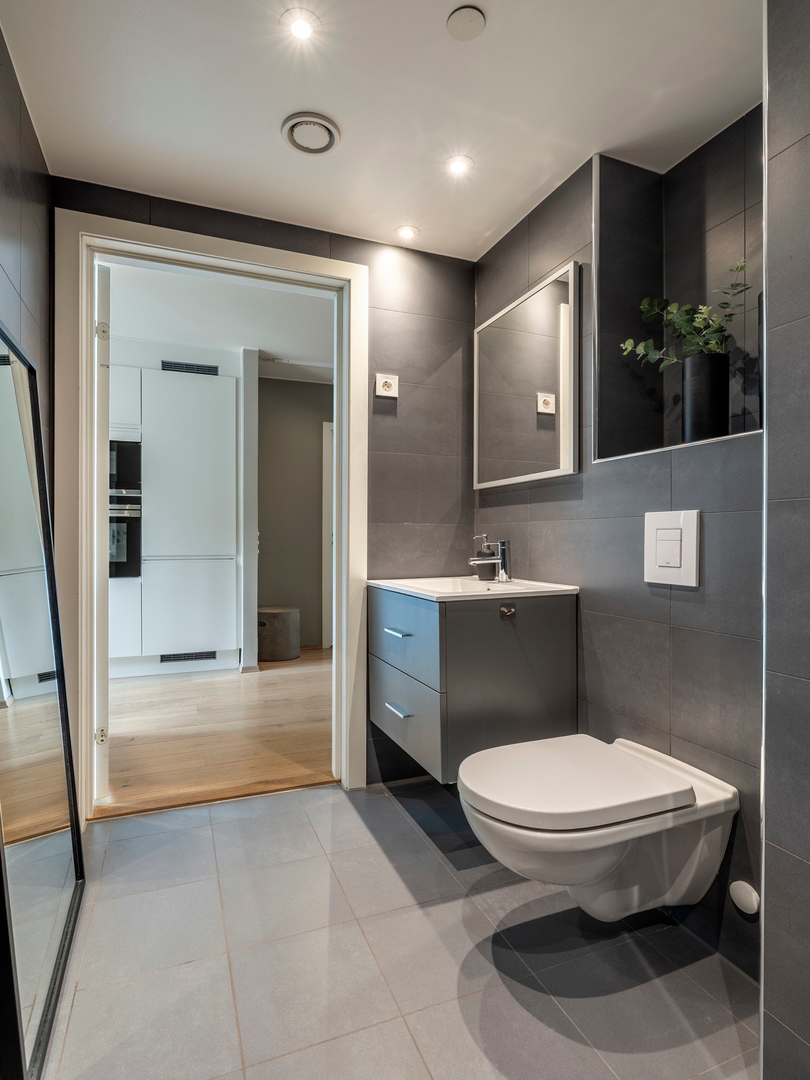 Innredet med servantinnredning, speil på vegg over servant, vegghengt toalett og dusjhjørne med svingbare glassdører. Galleribilde