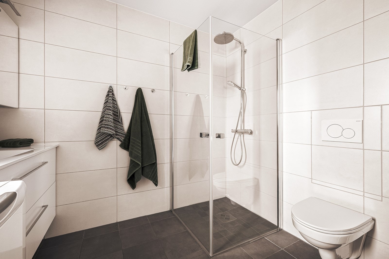 Pent og funksjonelt bad med fliser på vegger og gulv, dusjhjørne, vegghengt toalett og moderne innredning Galleribilde