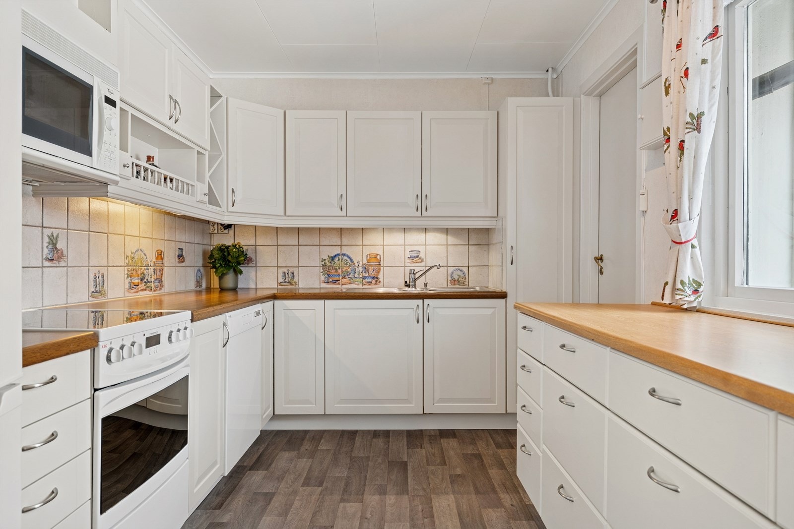 Kjøkken, innredning (ukjent årstall) med malte, profilerte fronter og laminert benkeplate. Over kokesonen er det mekanisk avtrekk og montert komfyrvakt. Det er ikke montert vannstoppersystem i kjøkkenbenk. Galleribilde