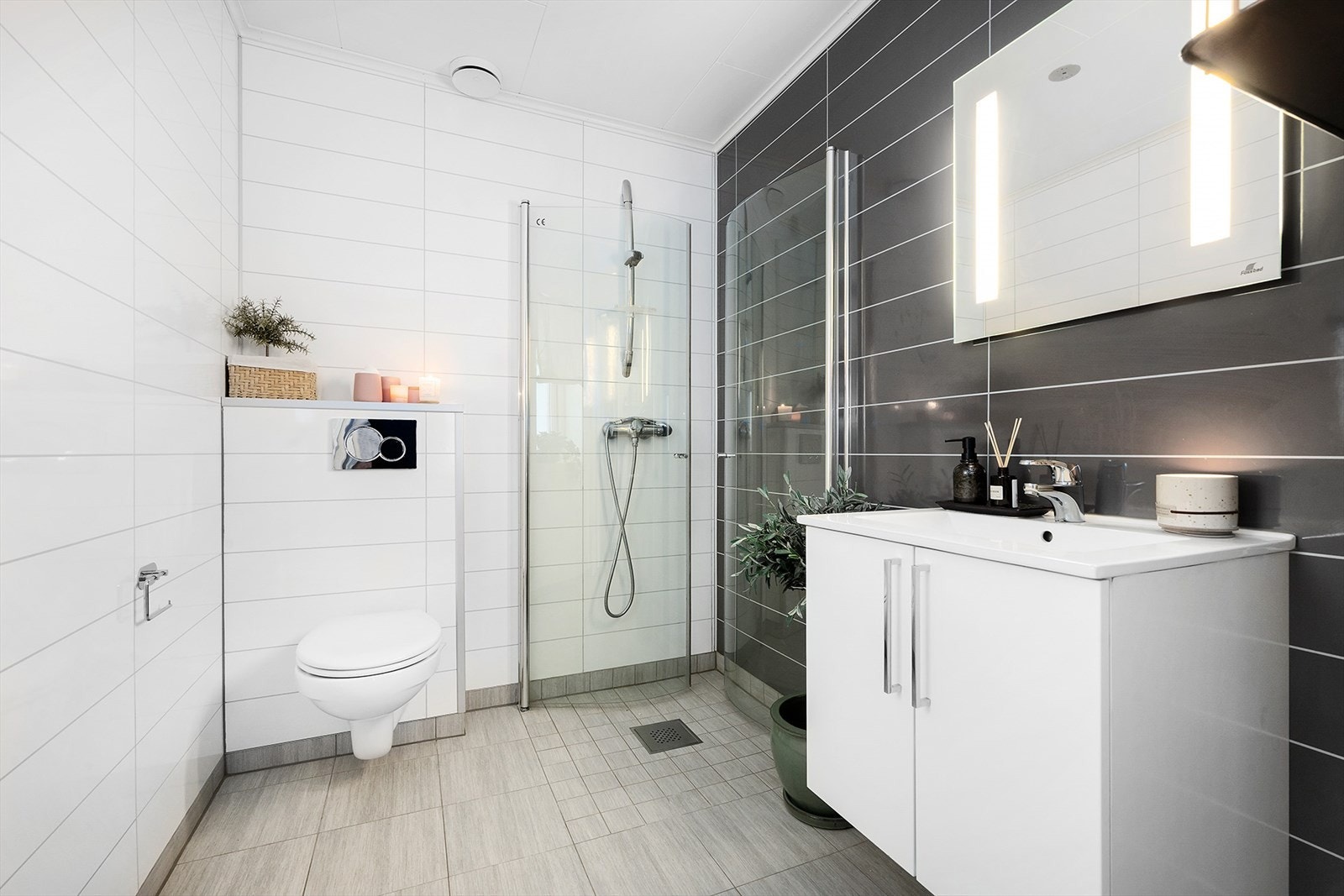 Badet i 1. etasje har flislagt gulv og baderomsplater på veggen, og er innredet med nedfelt servant, underskap og speil med lys. Galleribilde