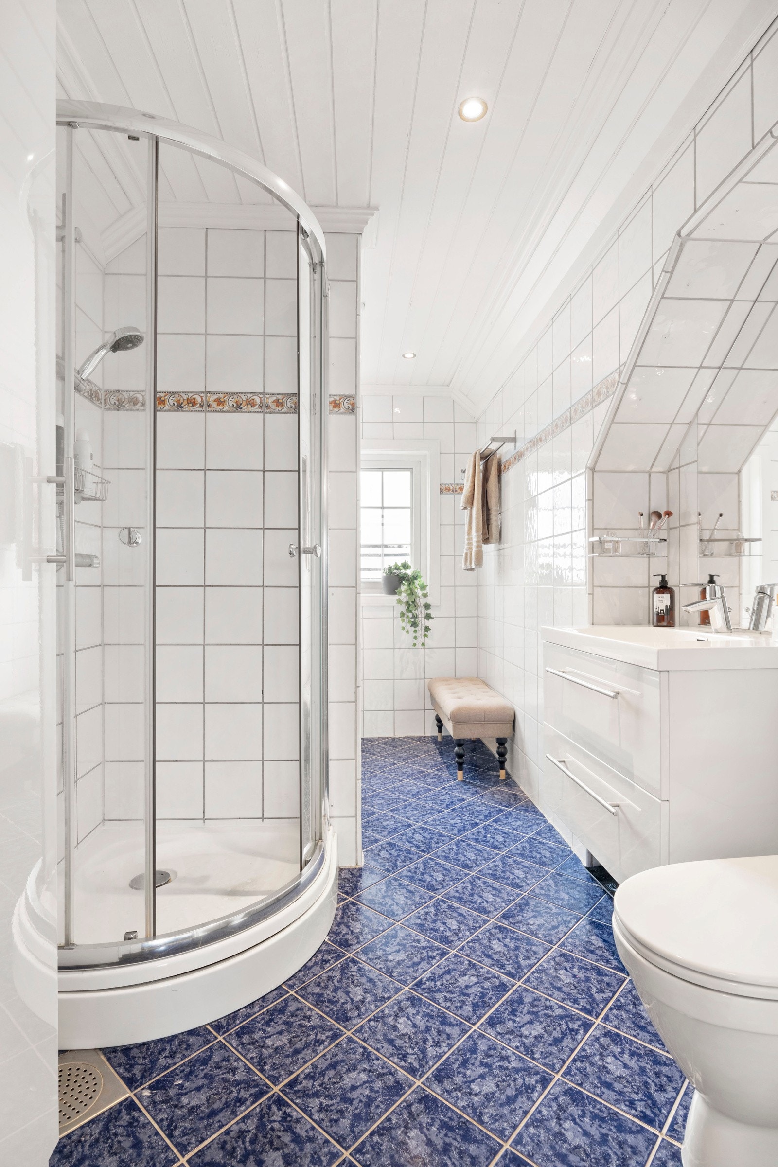 Flislagt bad med varmekabler i gulv og downlights i himling. Badet er innredet med toalett, dusjhjørne med kabinettgulv, badekar, servant integrert i skuffeinnredning og speil Galleribilde