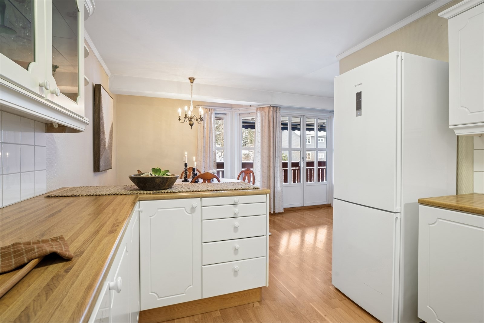 Klassisk kjøkkeninnredning med profilerte fronter, enkelte overskap med glass og en laminat benkeplate med nedfelt stålvask Galleribilde