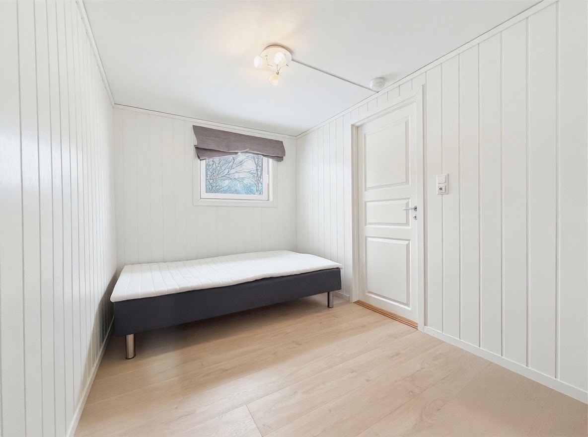Soverom med plass til seng og garderobe, lyse panelvegger og vindu Galleribilde