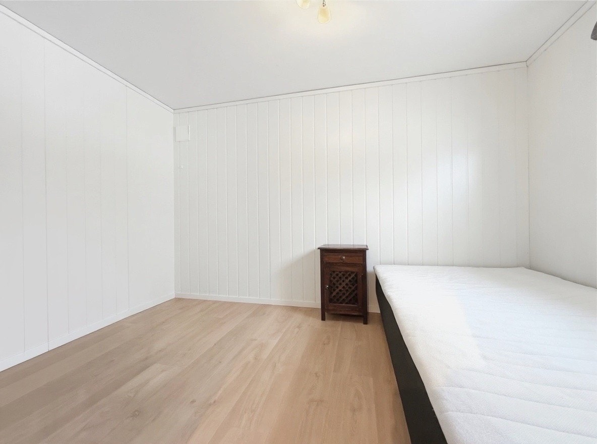 Soverom med plass til seng og garderobe, lyse panelvegger og vindu Galleribilde