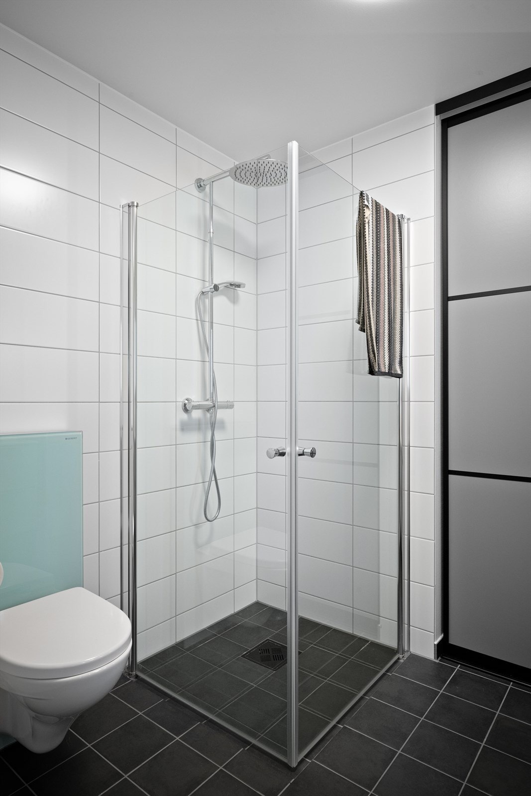 Flislagt baderom med opplegg for vaskemaskin, vegghengt toalett og baderomsinnredning Galleribilde