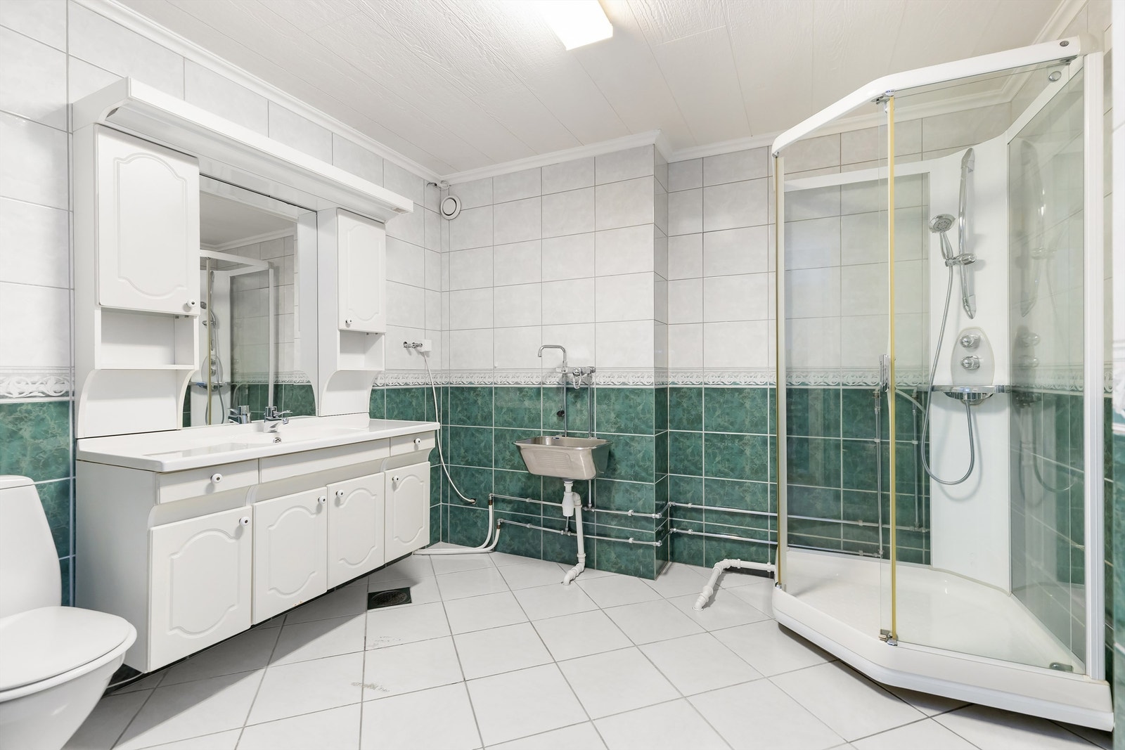 Badet er helfliset og utstyrt med dusjkabinett, servant med underskap og en praktisk utslagsvask. Galleribilde