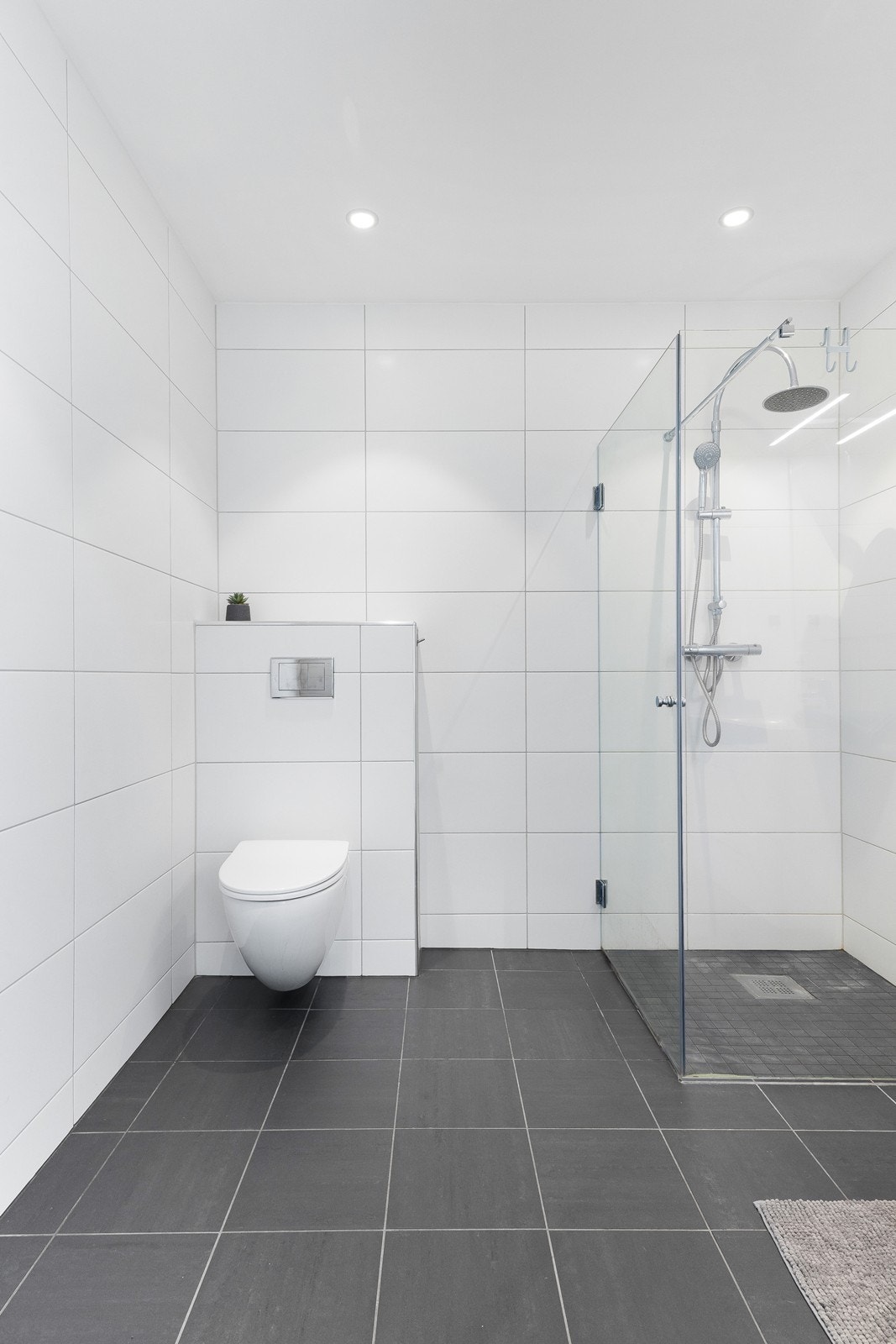 Stilrent helfliset bad som inneholder dusj, vegghengt toalett og baderomsseksjon med vask og skap. Galleribilde