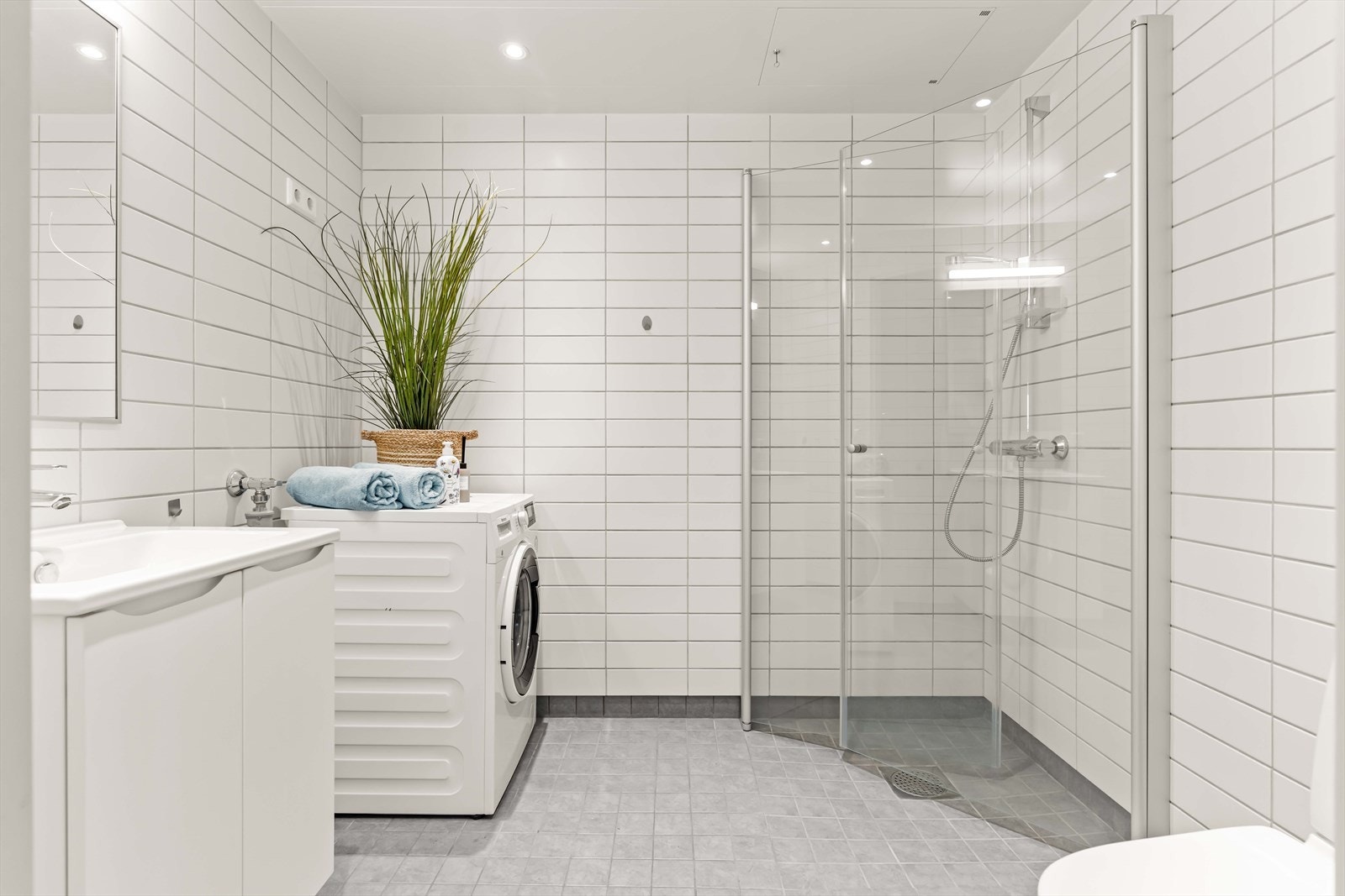 Stilrent bad med flislagte vegger og gulv, samt hvite stålplater med downlights i himlingen. Galleribilde