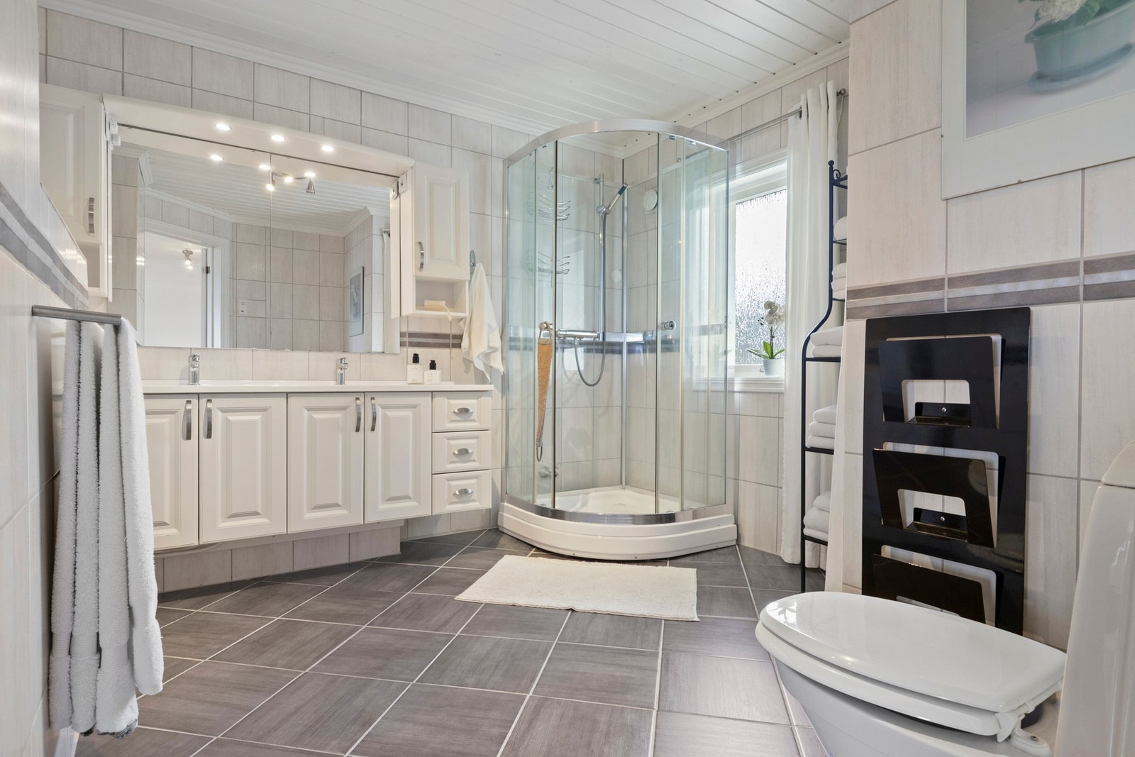 Badet har god størrelse og er innredet med lyse fliser i ulike gråtoner. Galleribilde