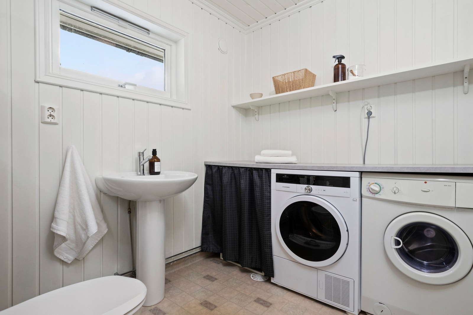 WC-rommet har gulvbelegg, søyleservant og en praktisk arbeidsbenk med tilhørende hylle. Under benken er det opplegg for vaskemaskin og plass til tørketrommel. Galleribilde