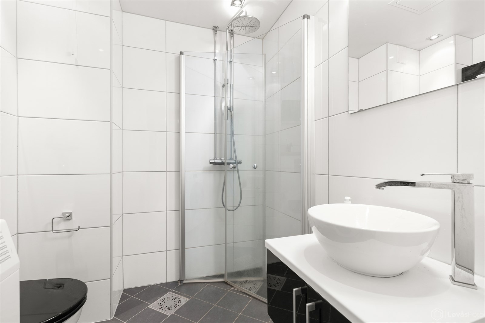 Lyst flislagt bad med dusjhjørne, servant med innredning, speil m/belysning, veggmontert toalett, samt veggskap over wc. Varmekabler i gulv. Galleribilde