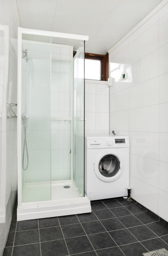Pent, flislagt bad med moderne dusjkabinett og praktisk opplegg for vaskemaskin Galleribilde