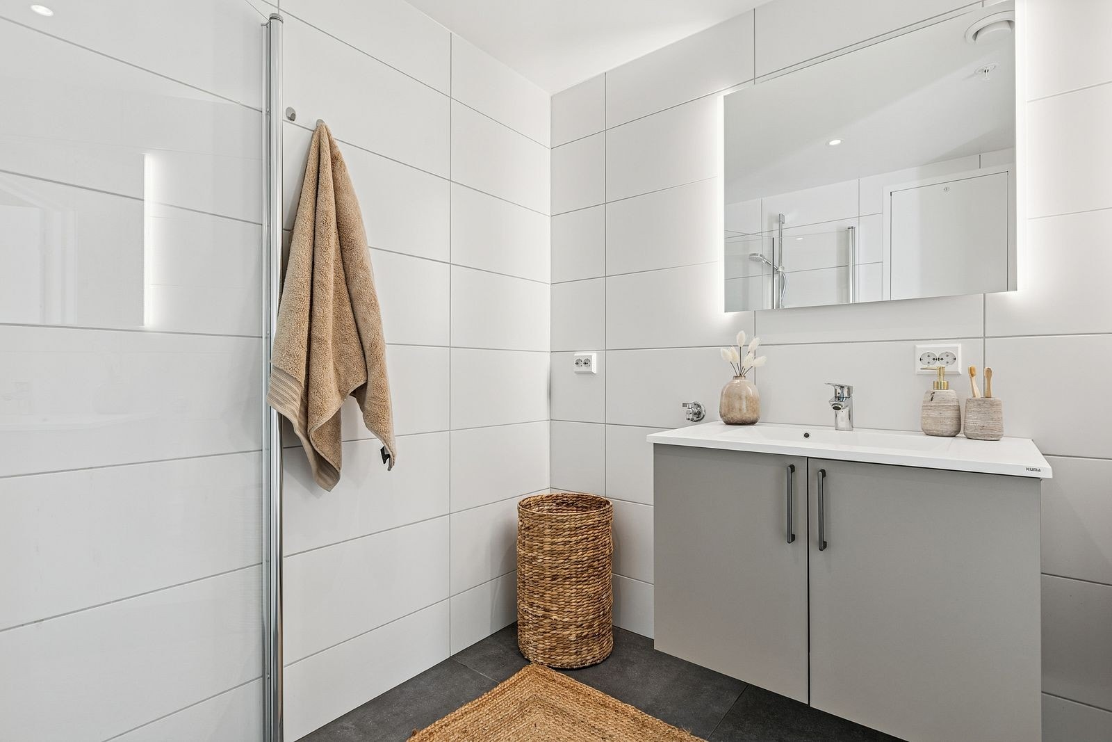 Innbydende baderom utstyrt med dusjhjørne med innfellbare dusjdører, vegghengt toalett, servantinnredning fra HTH, speil med lys og opplegg for vaskemaskin. Galleribilde