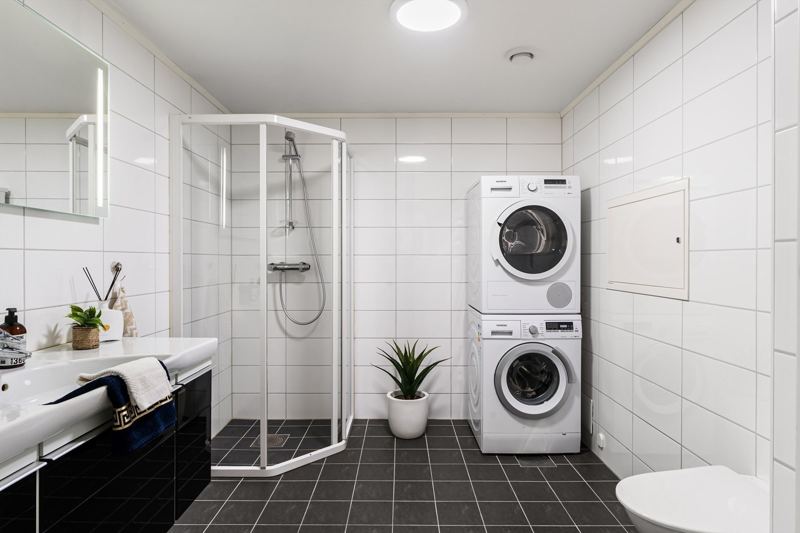 Helfliset bad med dusjnisje, vegghengt WC og servant i møbel og opplegg for vaskemaskin Galleribilde