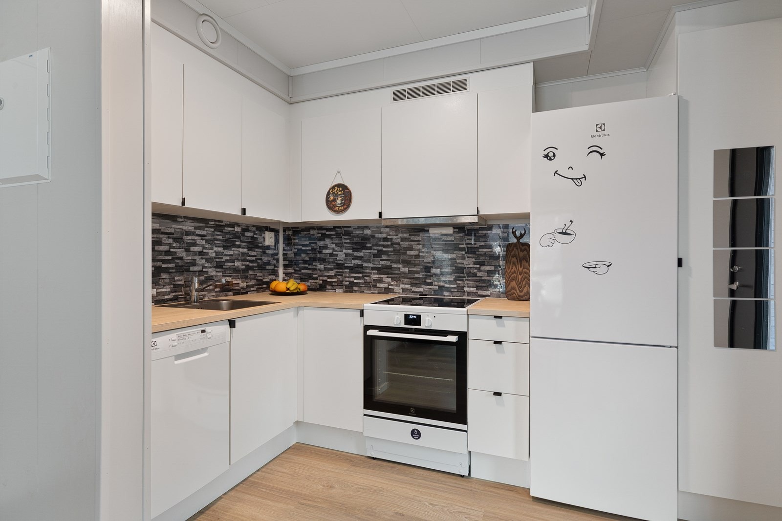 Kjøkken med innredning i glatt kvit utføring med benkeplate i laminat med nedfelt kum.
Friitståande kvitevarer som oppvaskmaskin, komfyr og kjøl/frys Galleribilde