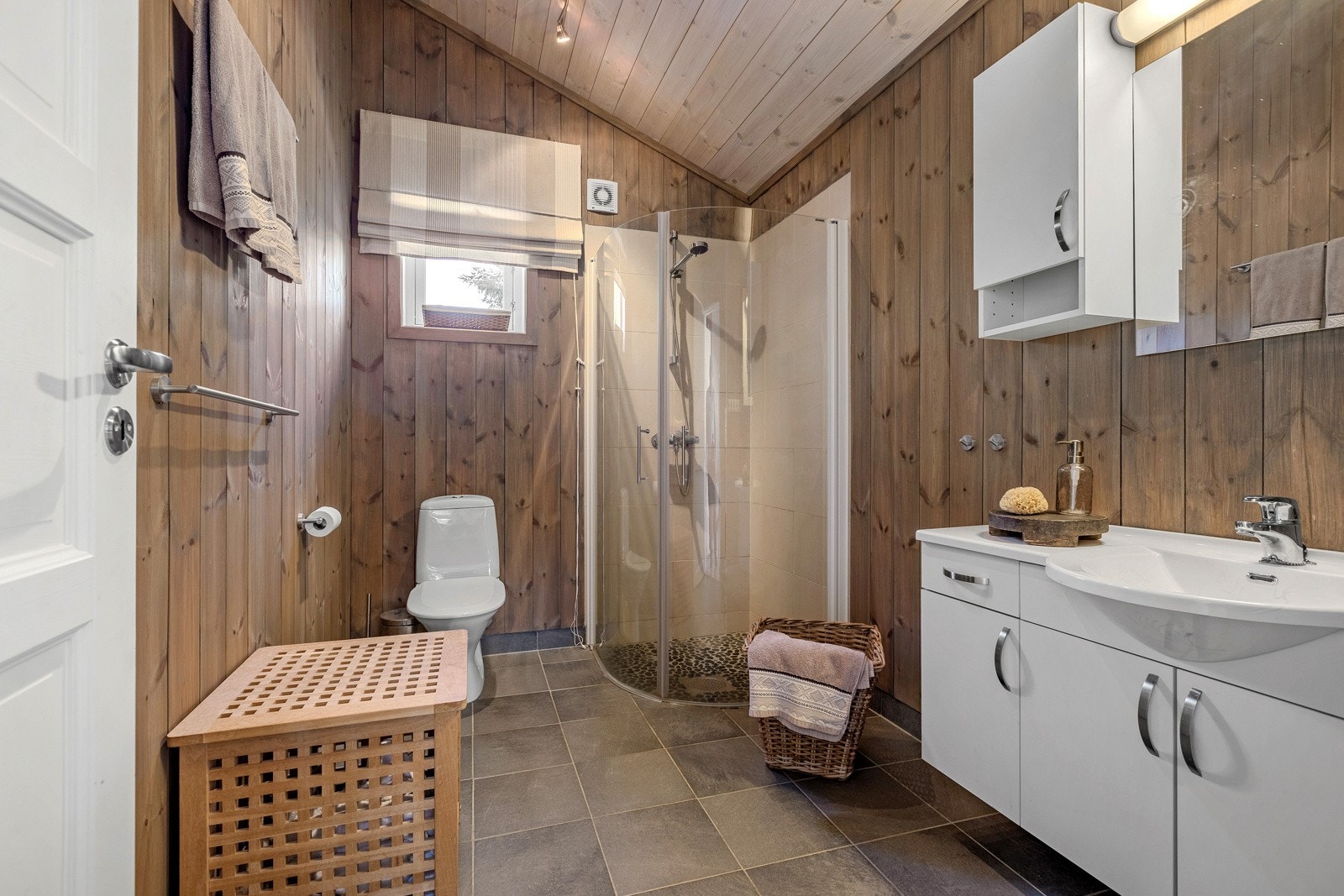 Badet er utstyrt med innredning som inkluderer en nedfelt servant, toalett og dusjvegger i et dusjhjørne. Galleribilde