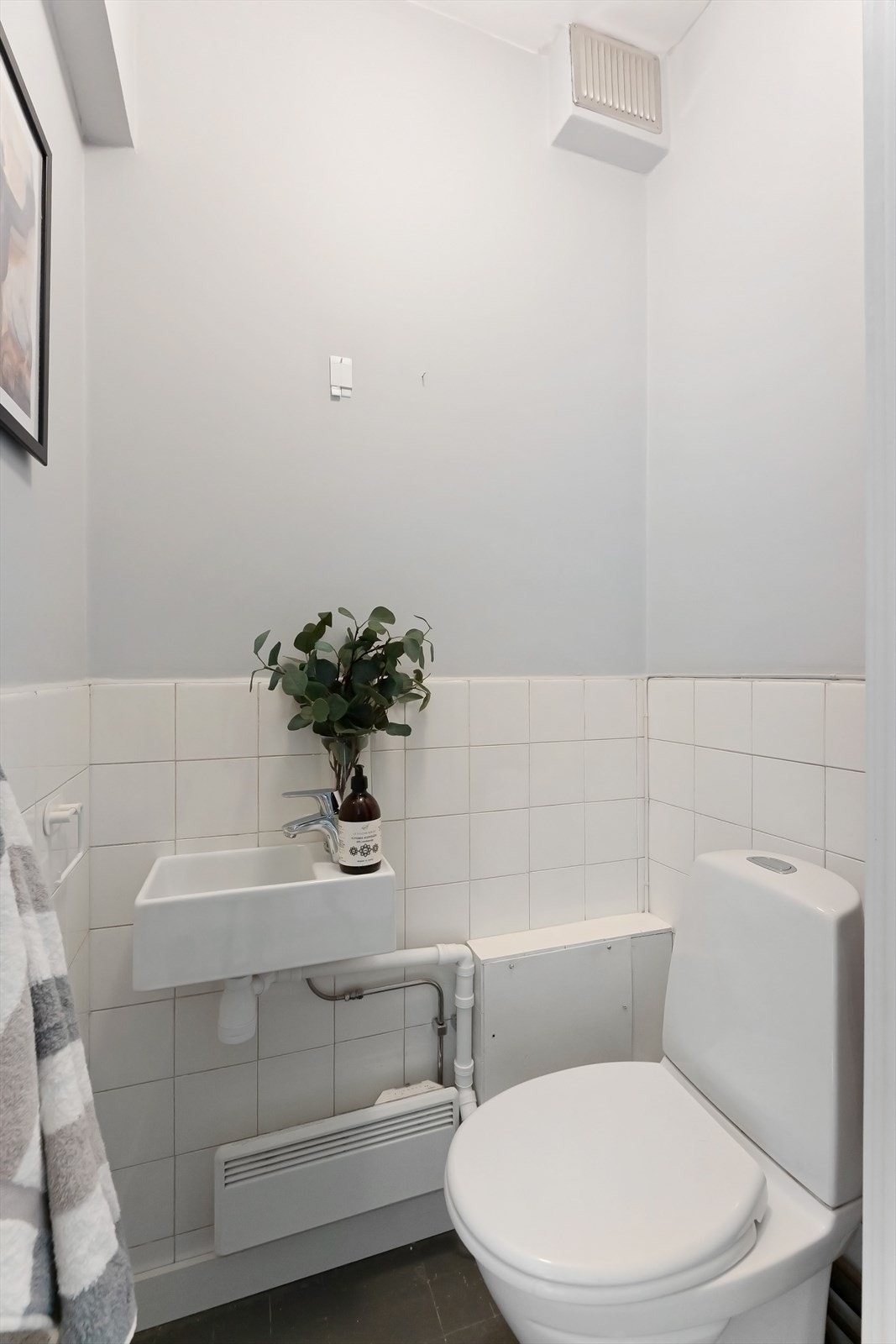 Separat toalettrom/WC med malt fliselagt gulv. Innredningen består av en servant med ettgreps blandebatteri og et gulvmontert toalett. Oppvarming skjer via en elektrisk panelovn, og rørene er utenpåliggende. Galleribilde