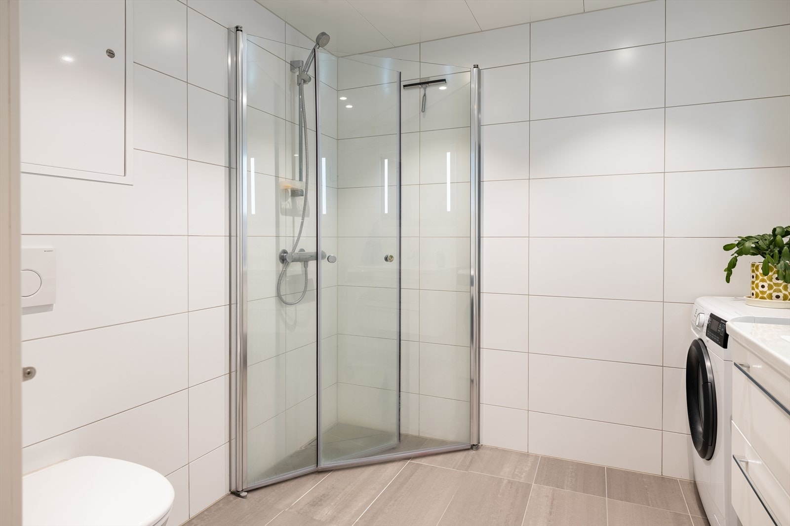 Badet er utstyrt med innfellbare dusjdører, mekanisk avtrekk, servantskap, veggmontert wc og rørfordelingsskap. Galleribilde