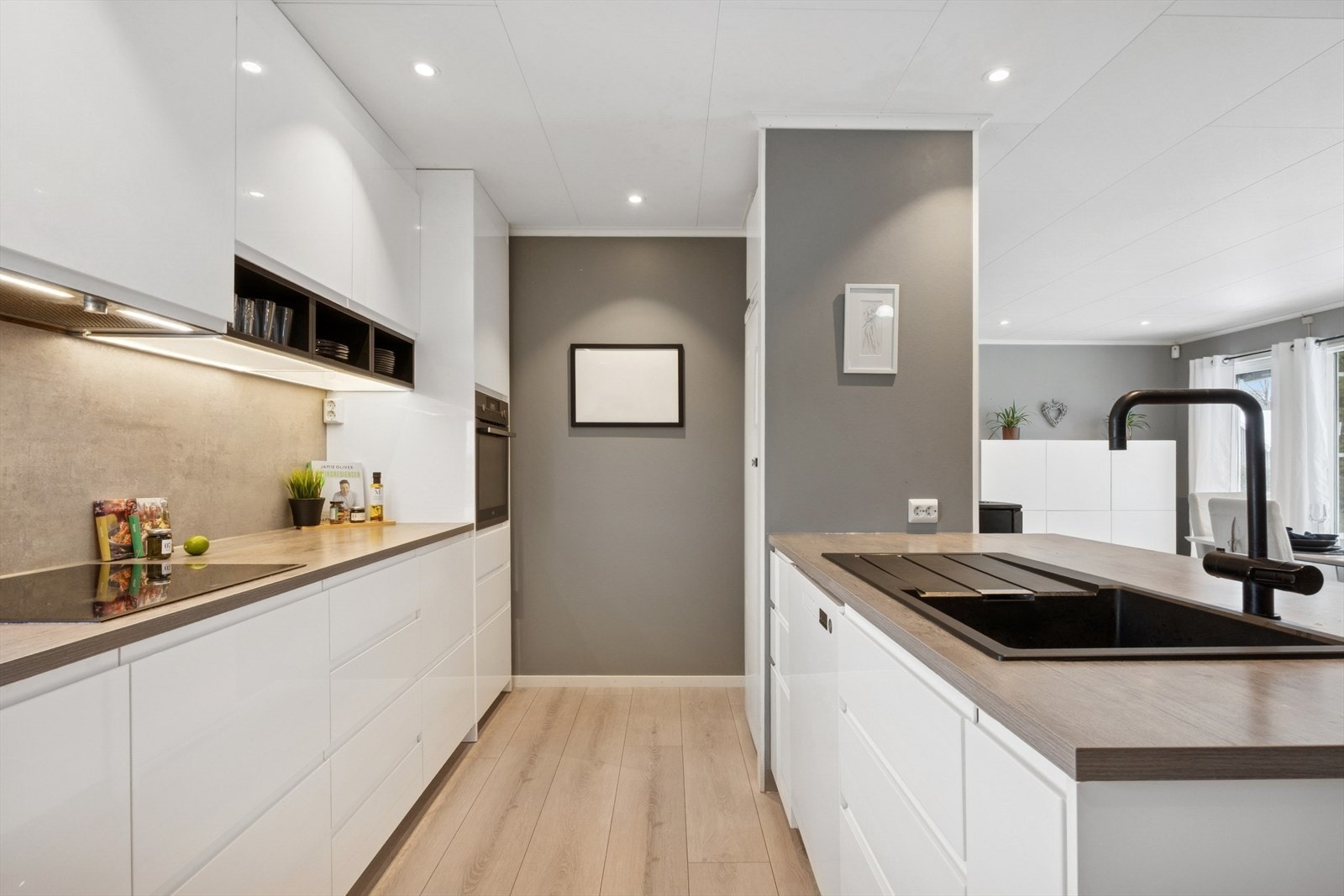 Kjøkkeninnredningen har hvite, glatte fronter og laminatbenkeplate med nedfelt oppvaskkum i sort kompositt. Galleribilde