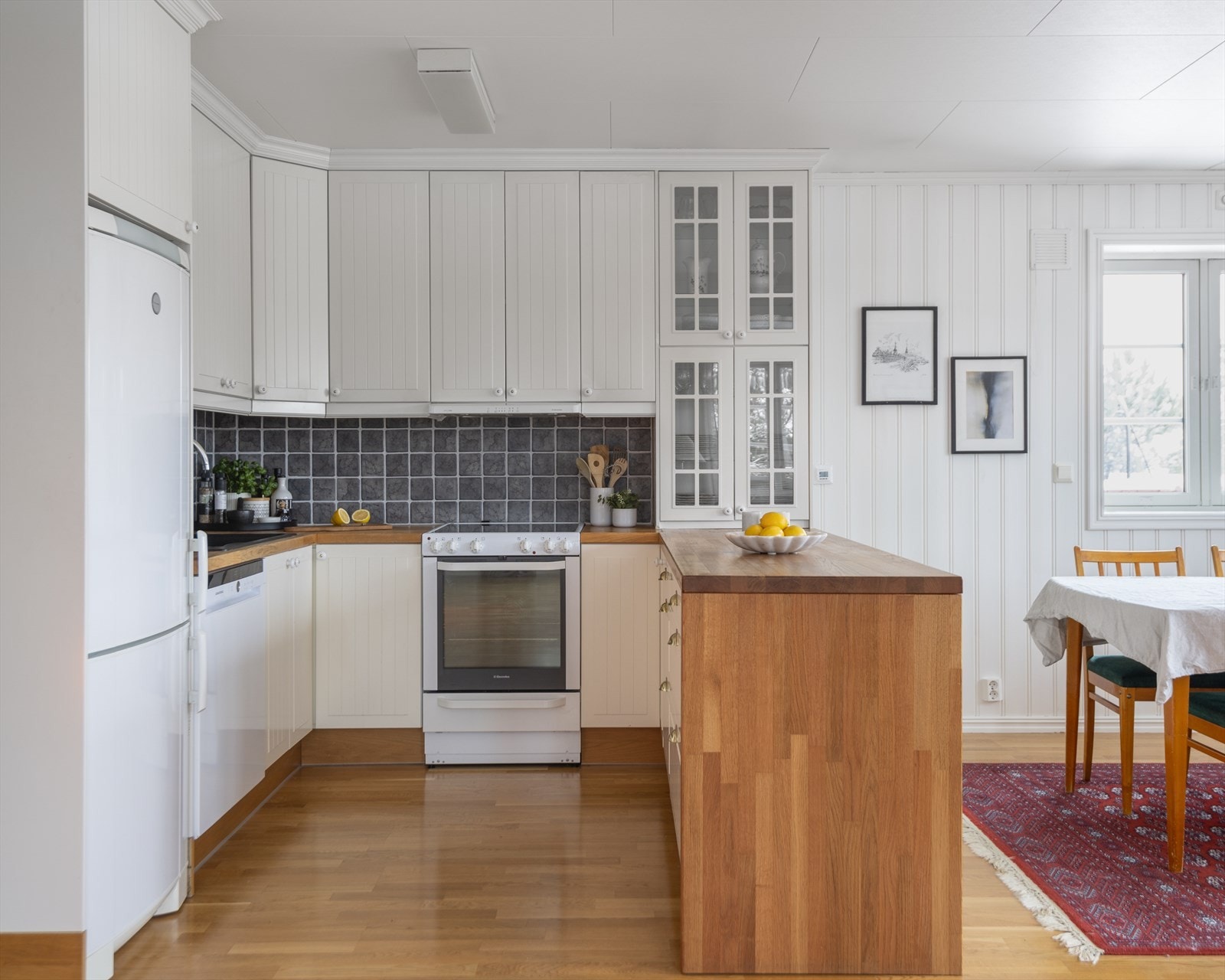 Den takhøye innredningen har hvite, profilerte fronter, vitrinedører og solid heltre benkeplate med nedfelt kum i kompositt. Galleribilde