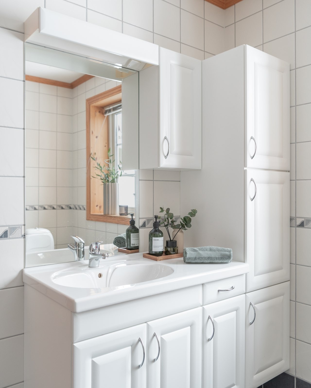 Innredningen har heldekkende servant over skapseksjon, matchende høy- og veggskap og speil med belysning. Galleribilde