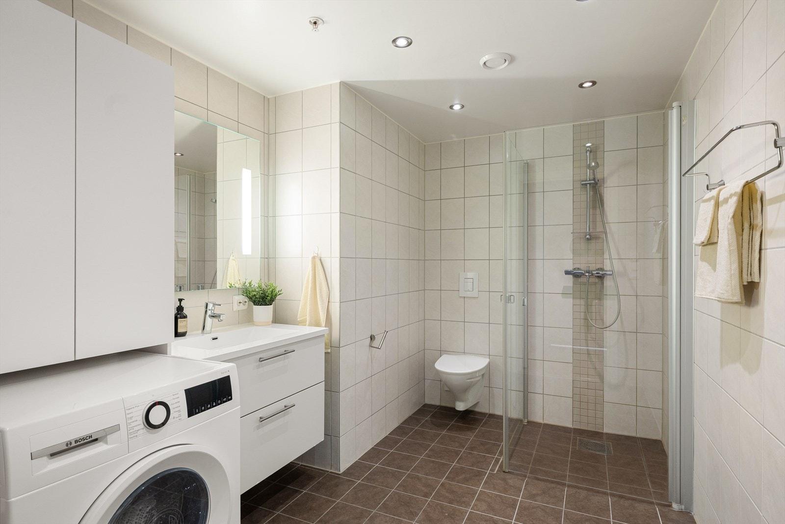 Badet er innredet med nedfelt servant, veggmontert toalett og dusjvegger/hjørne. Galleribilde