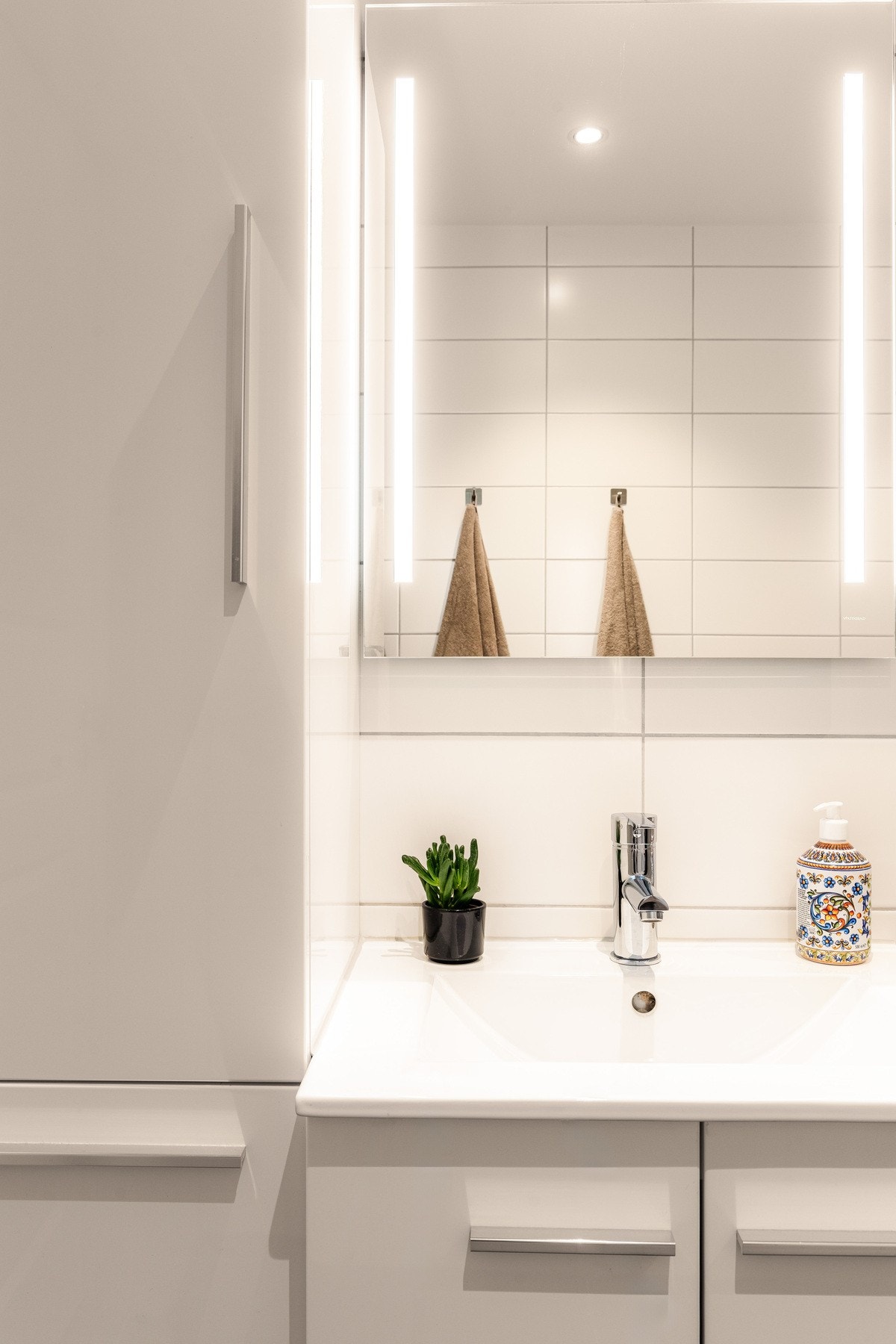 Badet er innredet med vegghengt servantskap med heldekkende servant og ettgreps armatur, speil med belysning, høyskap for ekstra oppbevaring samt vegghengt toalett. Galleribilde