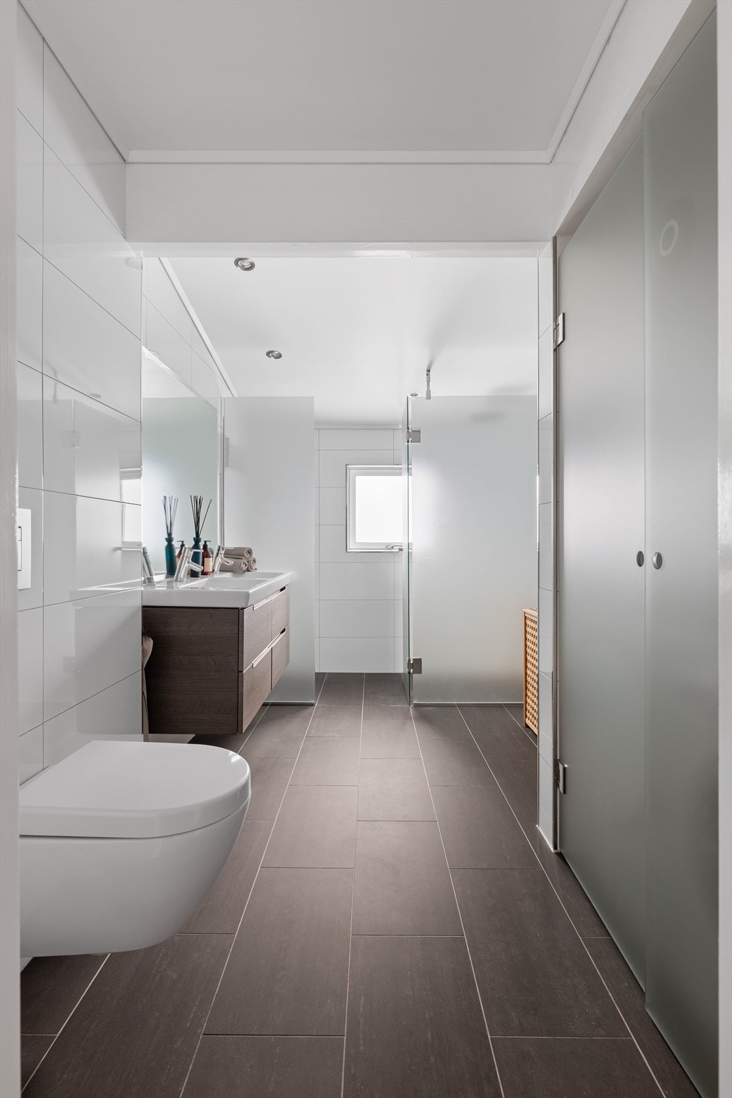 Badet er innredet med dusjhjørne med frostet glassvegg og regnfallsarmatur, veggmontert toalett, egen nisje for vaskemaskinn/tørketrommel og innredning med dobbel nedfelt servant Galleribilde