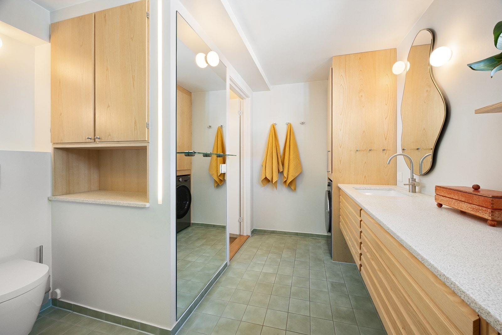 Baderomsinnredningen har gylne askefronter, lys Kuma steinkompositt benkeplate og underlimt porselensservant. Galleribilde