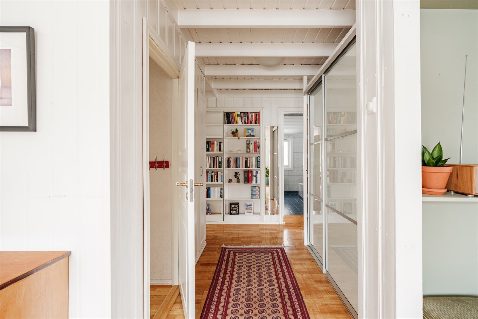 Mellomgang med gode lagringsmuligheter i skyvedørsgarderobe og bokhylle. Galleribilde