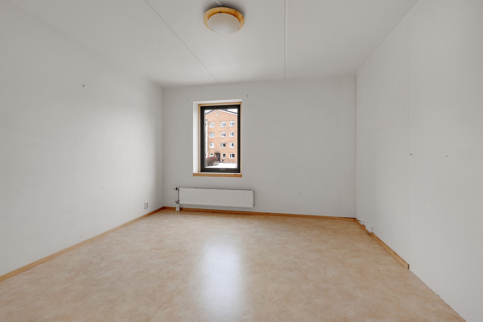 Rommet har lyse vegger og et vindu som gir naturlig lysinnslipp. Gulvet er belagt med vinyl, og det er en radiator under vinduet. Galleribilde