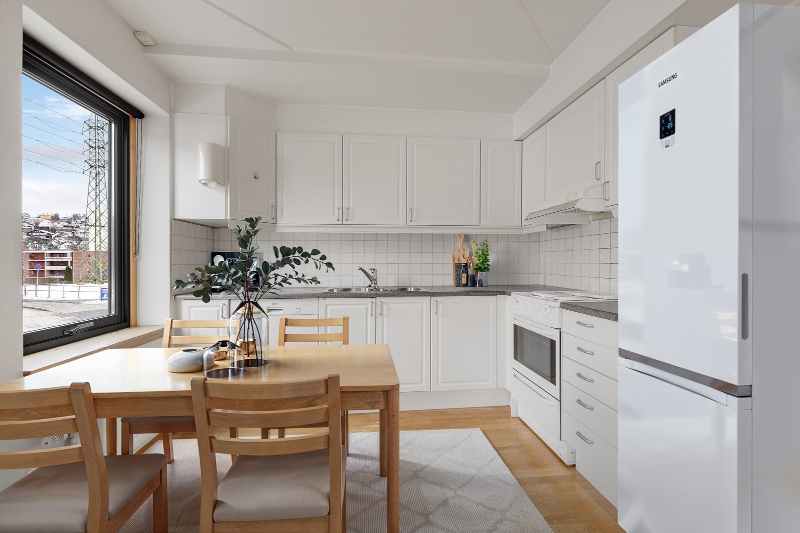 Hvite fronter og fliser gir et klassisk uttrykk på kjøkkenet, som er utstyrt med integrert oppvaskmaskin og komfyr. Bildet er digitalt stylet. Galleribilde