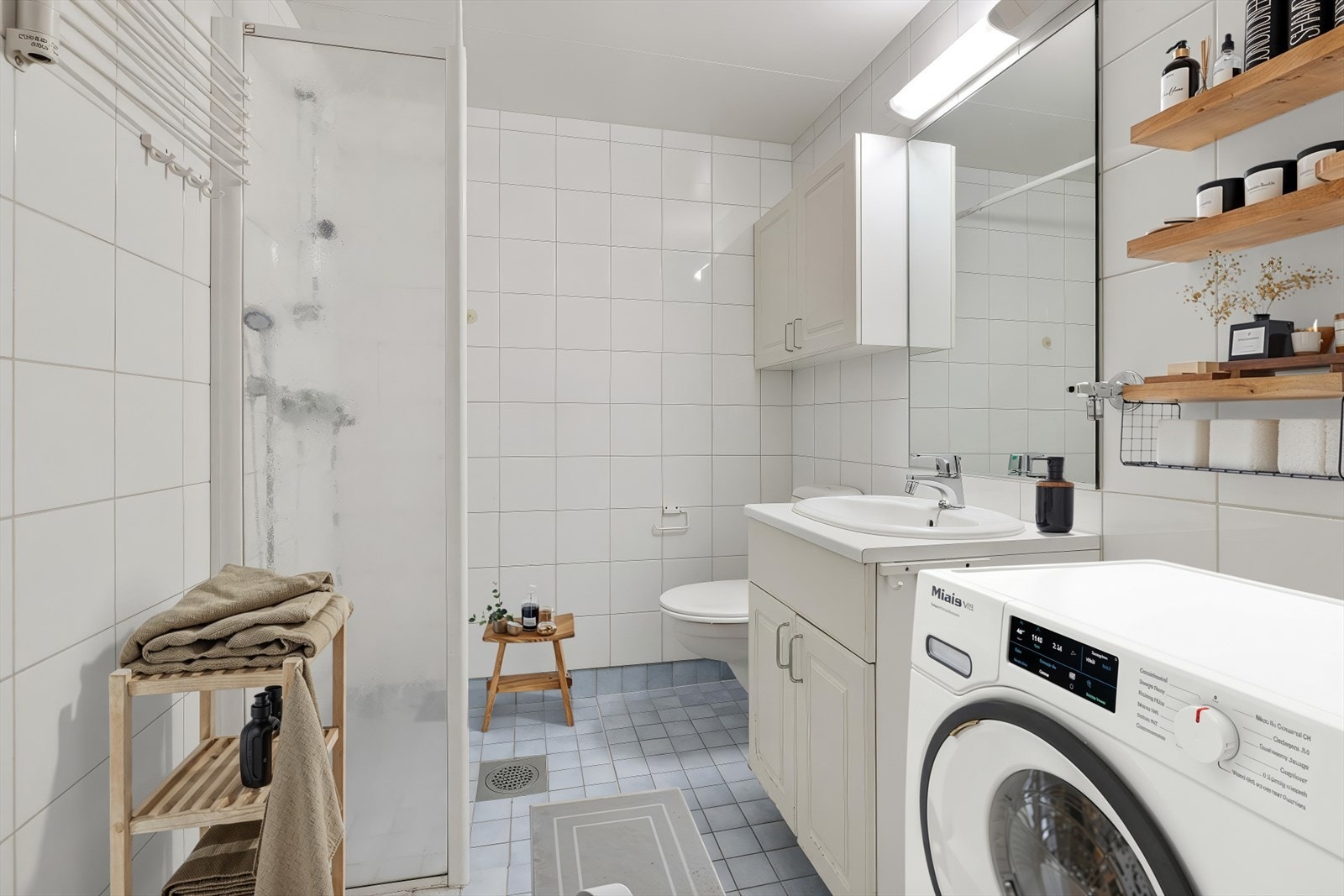 Flislagte vegger og gulv gir et tidløst uttrykk, mens servantskapet tilbyr praktisk oppbevaring. Bildet er digitalt stylet. Galleribilde