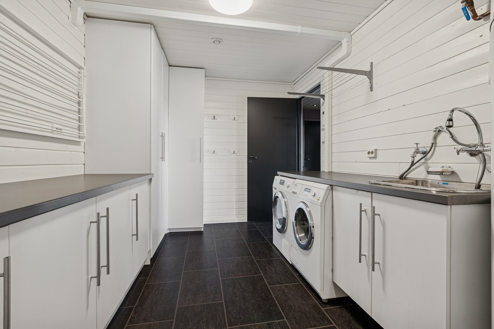Et stort og praktisk vaskerom med panel på veggene og belegg på gulvet. Rommet er innredet med vaskeromsinnredning med nedfelt skyllekar. Dør med direkte adkomst til bod. Galleribilde