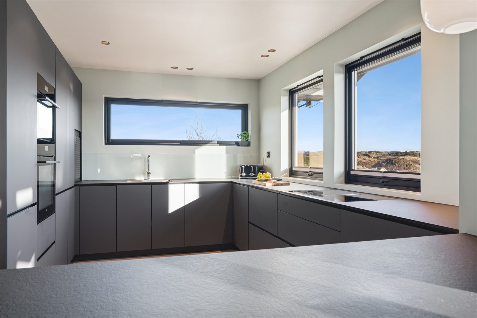 Stilrent KVIK kjøkken med mørke, glatte fronter og laminert benkeplate (innredningen er av nyere alder). Godt med skap- og benkeplass. Galleribilde