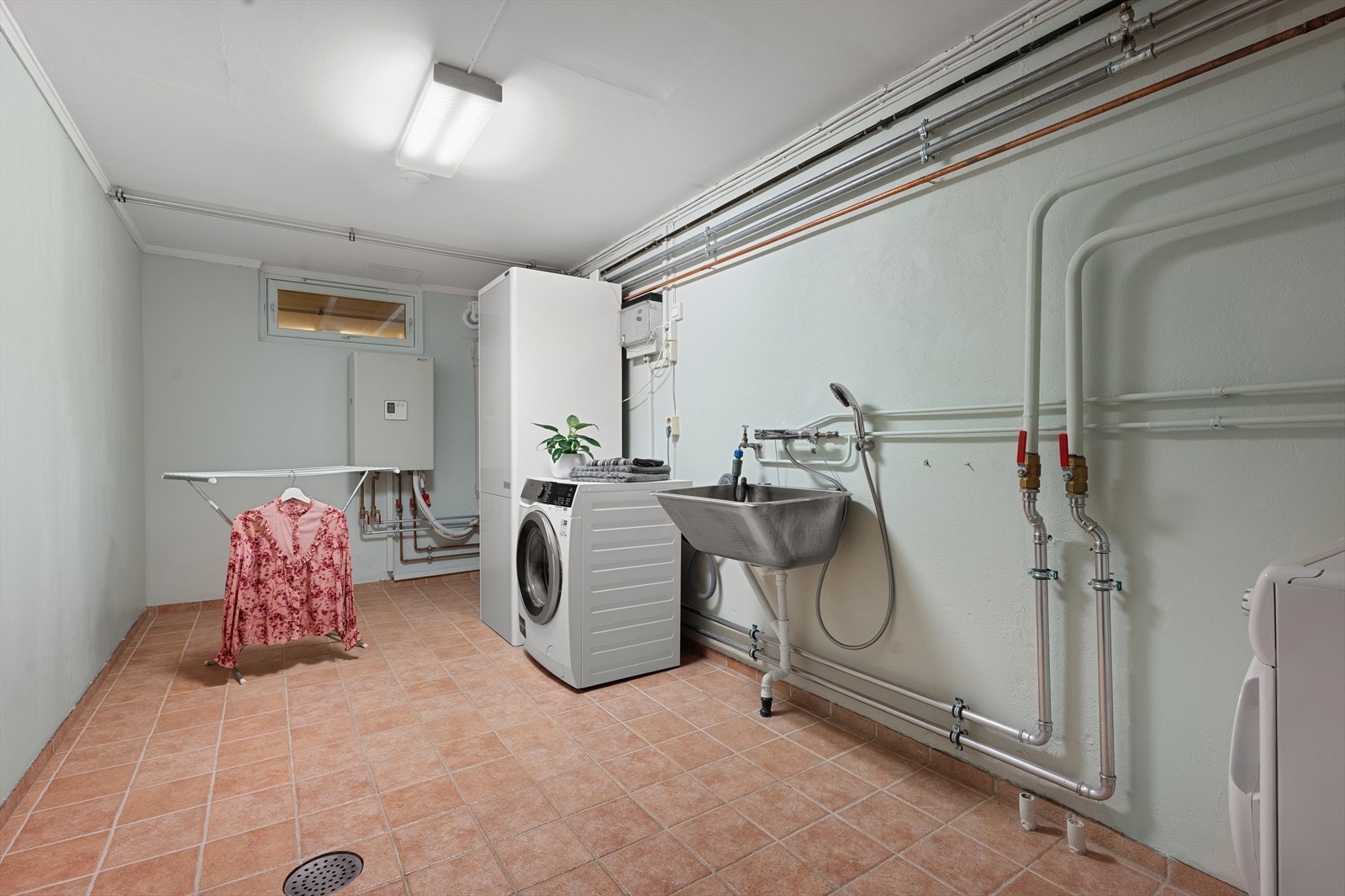 Stort teknisk rom/vaskerom med opplegg for vaskemaskin. Her er også boligens luft-til-vann varmeanlegg plassert. Galleribilde