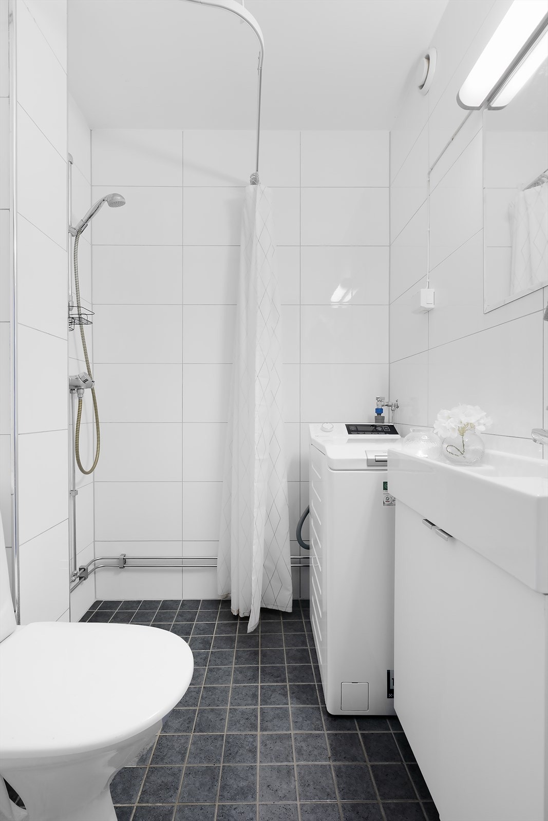 Flislagt bad med dusjhjørne, servant med underskap og speil over, WC og opplegg for vaskemaskin. Galleribilde