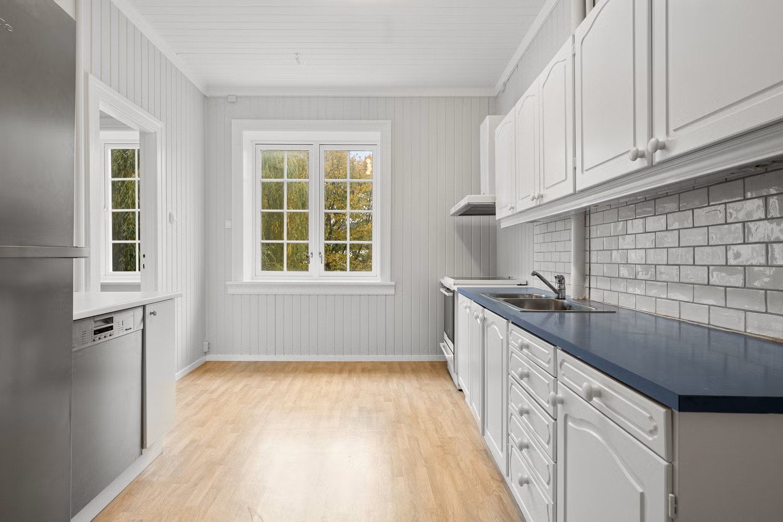 Kjøkken i heltre med fryseskap, kjøleskap, oppvaskmaskin, komfyr og sentralt avtrekk. Galleribilde