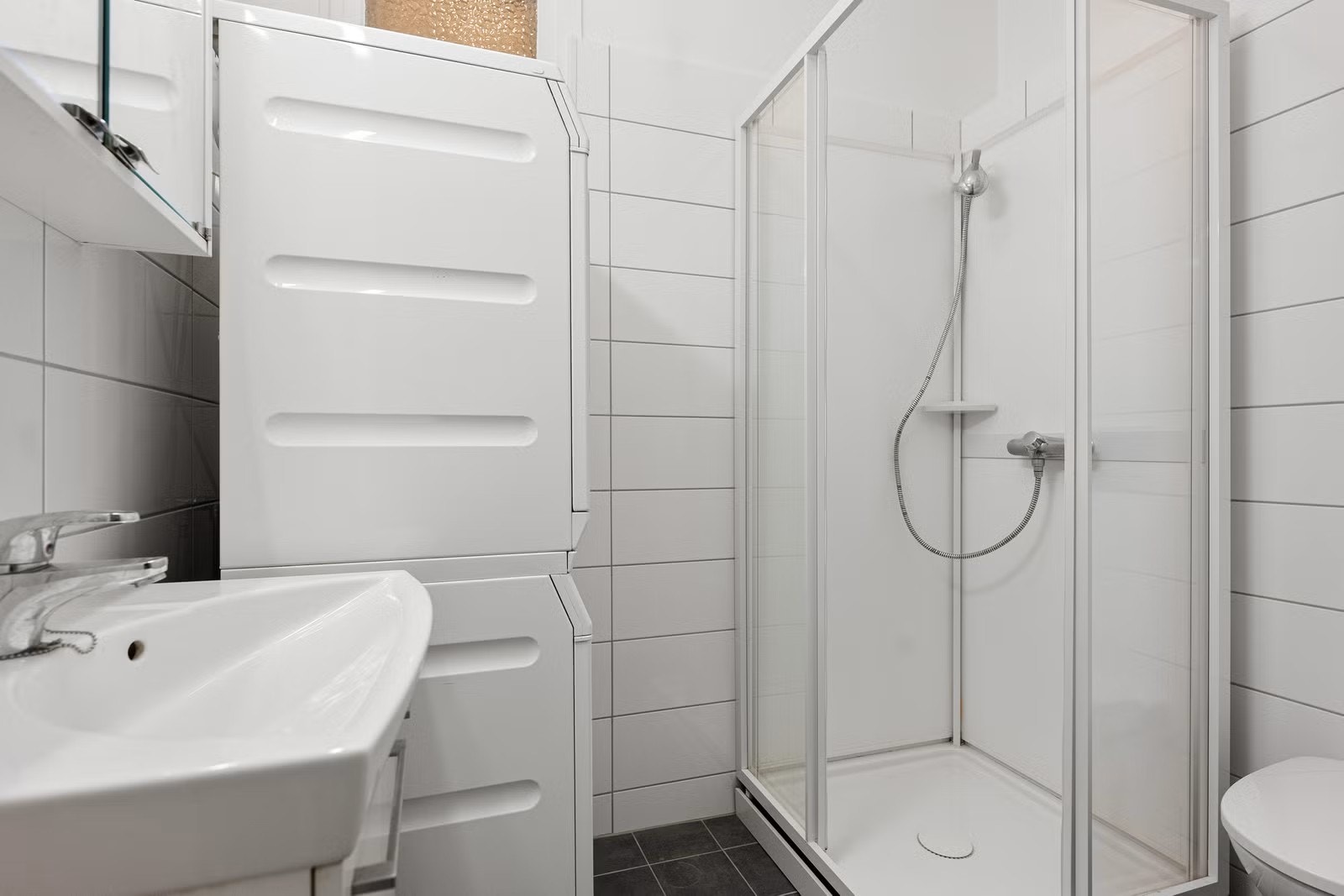 Bad med vaskemaskin, tørketrommel, dusjkabinett, servant og toalett. Det er varmekabel i gulvet. Galleribilde