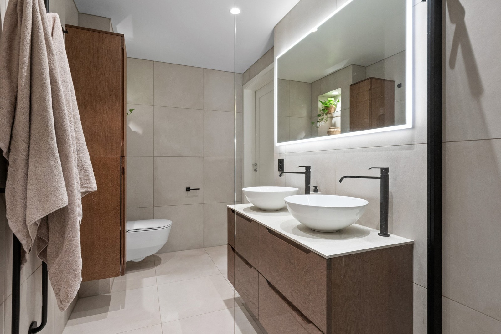 Badet inneholder innredning med skuffer og to servanter, veggmontert toalett, dusjvegg og speil med varme. Galleribilde