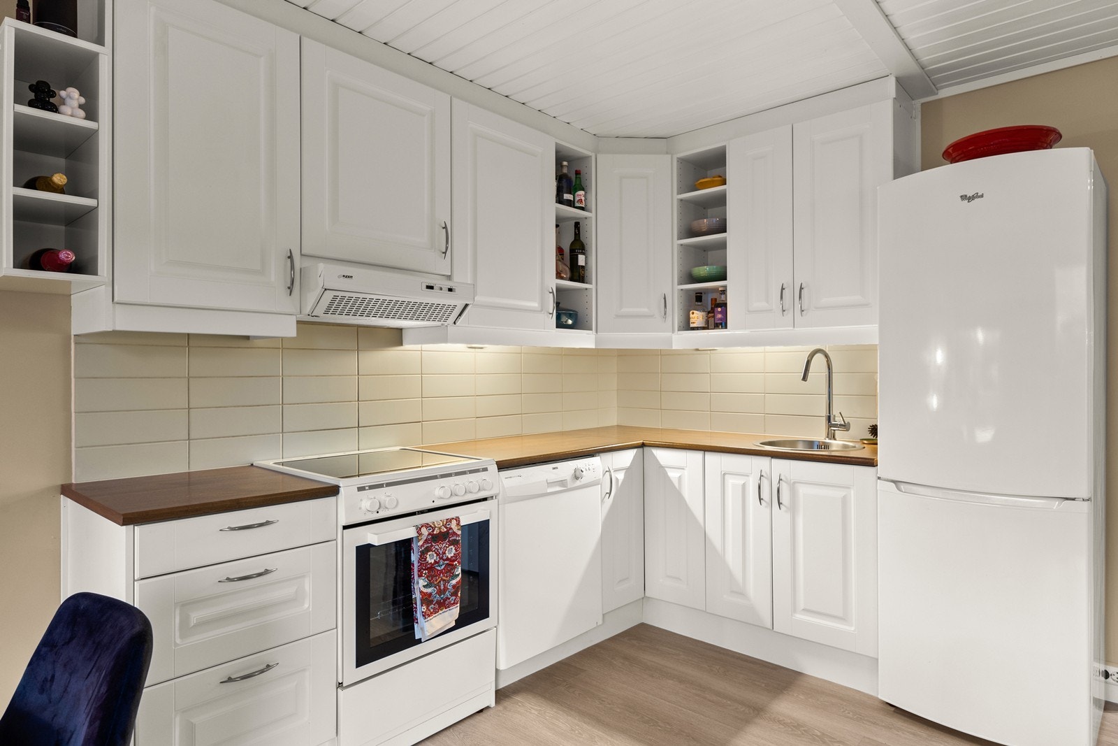 Innredning i L-form med hvite profilerte fronter og fliser på vegg Galleribilde