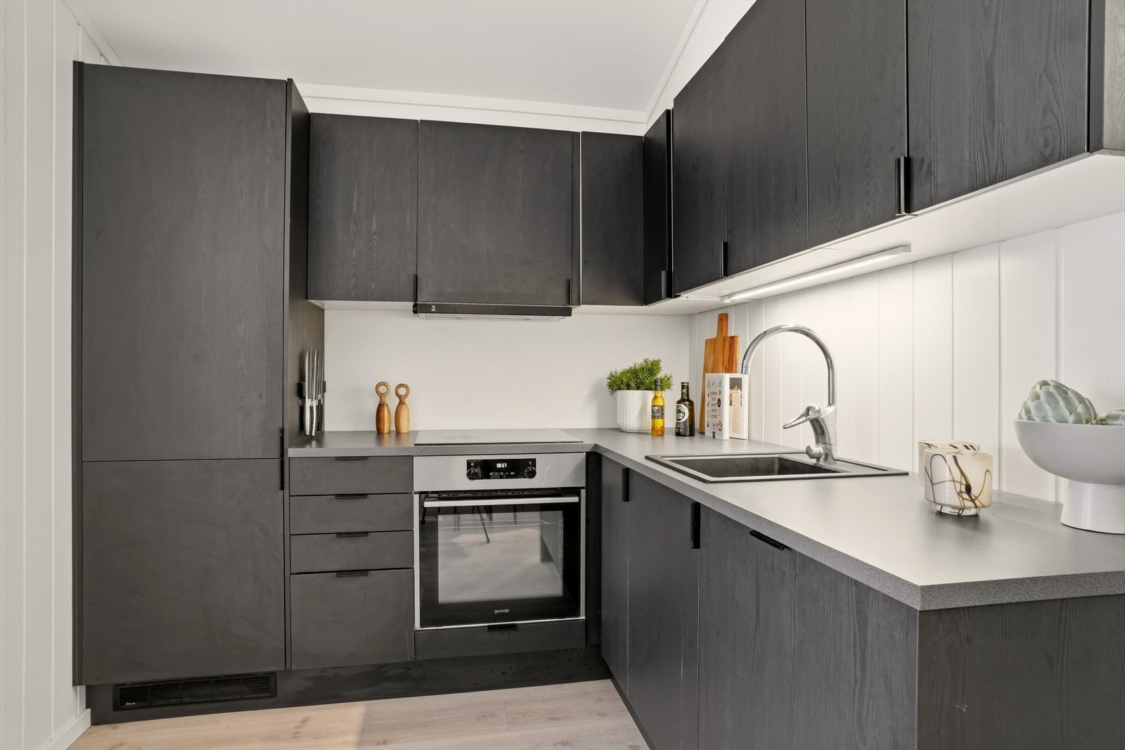 De mørke frontene gir et eksklusivt preg og står i flott kontrast til de lyse veggene og benkeplaten. Løsningen er arealeffektiv og smart utnyttet, med god skap- og benkeplass. Galleribilde