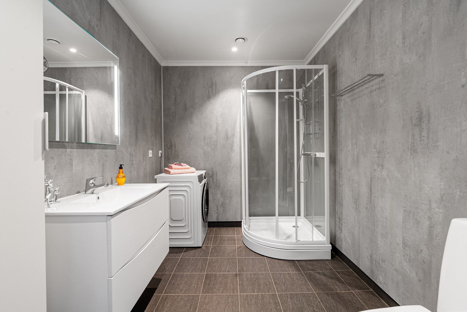 Badet har innredning med dype skuffer og høyskap, samt speil med integrert belysning. Badet er også innredet med dusjkabinett og toalett. Galleribilde