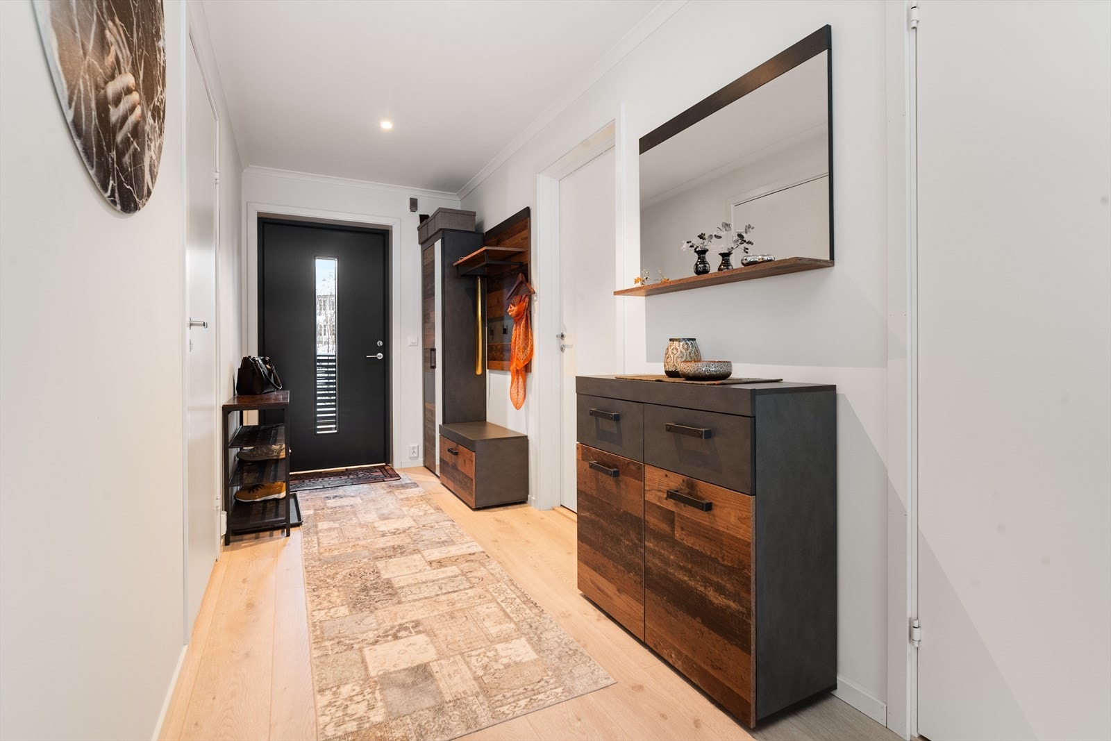 Med adkomst fra overbygget svalgang kommer man inn i boligens romslige gangareal hvor det er lyse, fine overflater og moderne parkettgulv. Disse overflatene er gjennomgående for leiligheten og gir et delikat og helhetlig inntrykk. Galleribilde